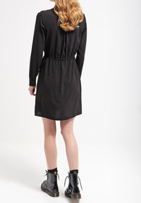 Svart långärmad klänning med åtdragen midja och rak fåll. Matchad med glänsande svarta snörstövlar med tjock klack.