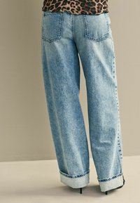 Vaalean siniset leveät farkut, joissa on haalistunut pinta, takataskut ja käärityt helmat, valmistettu denim-kankaasta, jossa on tekstuuri.