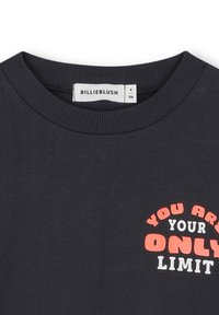 Zwart crewneck shirt met de tekst "JE BENT JE ENIGE BEPERKING" in rood en wit op de borst en een Billieblush-label binnenin de kraag.