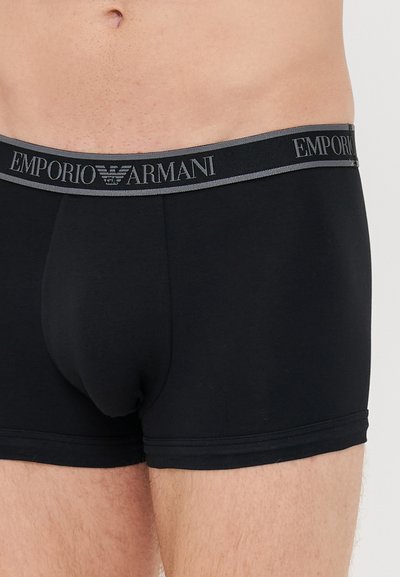 Schwarze Baumwoll-Boxershorts mit einem grauen Bund, auf dem das Logo "Emporio Armani" zu sehen ist. Glatte Textur und enge Passform an den Oberschenkeln.