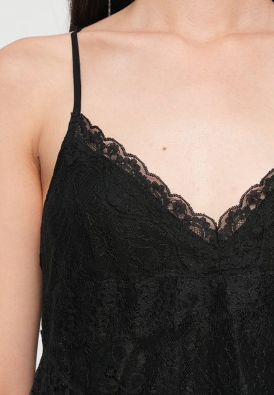 Camisole en dentelle noire avec des bretelles réglables, un décolleté festonné et un motif floral complexe sur un tissu transparent.