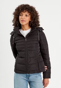 Veste matelassée noire avec texture capitonnée, fermeture éclair sur le devant, capuche réglable avec cordon de serrage, poches latérales et design ajusté.
