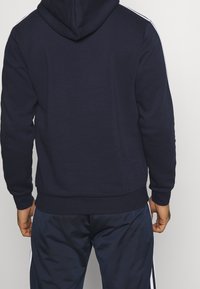 Hoodie bleu marine avec une bande blanche le long des manches, doté d'une capuche avec cordon de serrage et de poignets et ourlet côtelés pour un ajustement parfait.