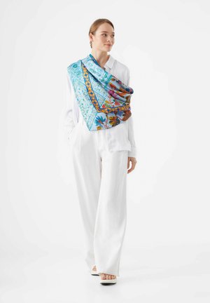 Leuchtend blaue Seidenschal mit floralem und geometrischem Muster, über einer weißen Bluse drapiert, mit Akzenten in Orange und Braun.