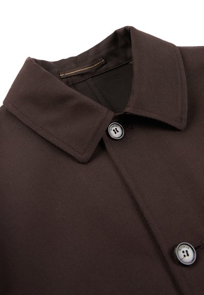 Brązowa koszula z kołnierzykiem, wykonana z teksturowanej tkaniny, z pojedynczym zapięciem na guzik i kontrastowym akcentem guzika na kołnierzu.