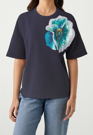 Marineblaues Kurzarm-T-Shirt mit großem floralen Design in Türkis, Weiß und Gelb auf der linken Seite. Glatte Baumwollstruktur, lockere Passform.