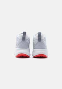 Ζεύγος γκρι και λευκών παπουτσιών για τρέξιμο με υφασμένα πέλματα και κόκκινα εξωτερικά πέλματα, εμφανίζεται από πίσω σε απλό φόντο.