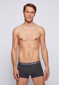 Dunkelgraue Boxershorts mit einem weißen "HUGO BOSS"-Logo auf dem elastischen Bund. Glattes Material, figurbetontes Design und Oberschenkel-Länge.