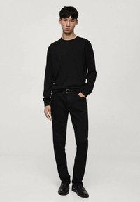 Camicetta nera a maniche lunghe e pantaloni neri skinny. La camicia presenta un collo rotondo, mentre i pantaloni hanno un design classico e una texture sottile. Le scarpe nere completano il look.