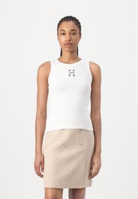 Weißes geripptes Tank-Top mit rundem Ausschnitt und kleinem schwarzem Logo. Getragen mit einem beigen strukturierten Rock mit silbernen Akzenten.