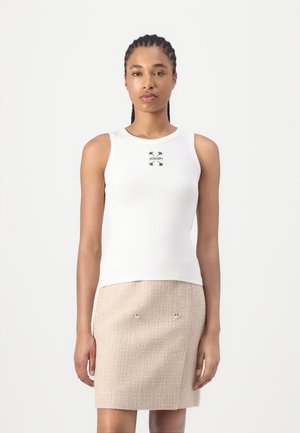 Hvit ribbet tanktopp med rund halslinning og en liten svart logo. Kombinert med et beige teksturert skjørt med sølvdetaljer.