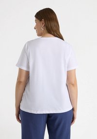 Camisa blanca de manga corta con un corte holgado, que presenta una textura sutil. Combinada con pantalones azul marino, que exhiben un diseño relajado.