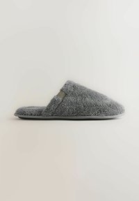 Gray fuzzy closed-toe slipper with a low back and a small fabric tag on the side, shown in profile on a plain background.