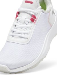 White athletic shoe with textured fabric upper, pink accents on the laces and logo, and a flexible sole. Rounded toe and padded collar.