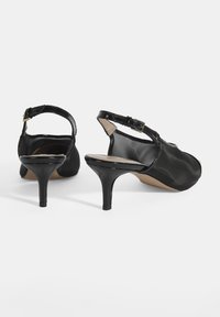 Chaussures à talons aiguilles noires à talon slingback avec une finition brillante, bout ouvert et un talon stiletto fin. Dispose d'une fermeture à boucle au niveau de la cheville.