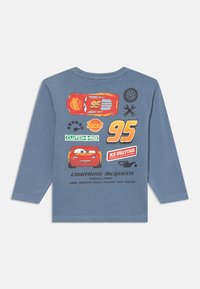 Hosszú ujjú kék póló, amelyen a Lightning McQueen grafikái láthatók, beleértve autós képeket és sárga, valamint fehér színű szöveget a hátsó oldalon.
