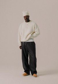 Hvid tekstureret sweater, løstsiddende sorte bukser, brune slip-on sko og en lys farvet beanie. Enkel lagdeling med minimale accenter.