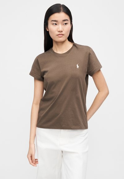 Barna rövid ujjú pamutpóló, környakú nyakkivágással és egy kis fehér logóval a bal mellrészen. Egyszínű textúra.