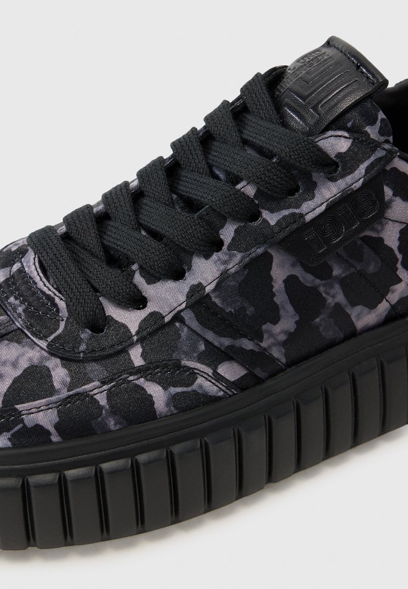 Schwarze und graue gemusterte Sneaker mit einer strukturierten Oberseite, dicker Gummisohle, flachen Schnürsenkeln und gepolsterter Knöchelunterstützung.