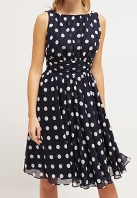 Marineblaues, ärmelloses Kleid mit weißen Punkten, gerafft an der Taille, fließender Rock, aus leichtem Stoff mit einer glatten Textur.