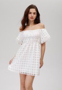 Robe blanche à épaules dénudées avec un motif en grille transparent, manches bouffantes, taille élastique et un tissu léger et fluide.