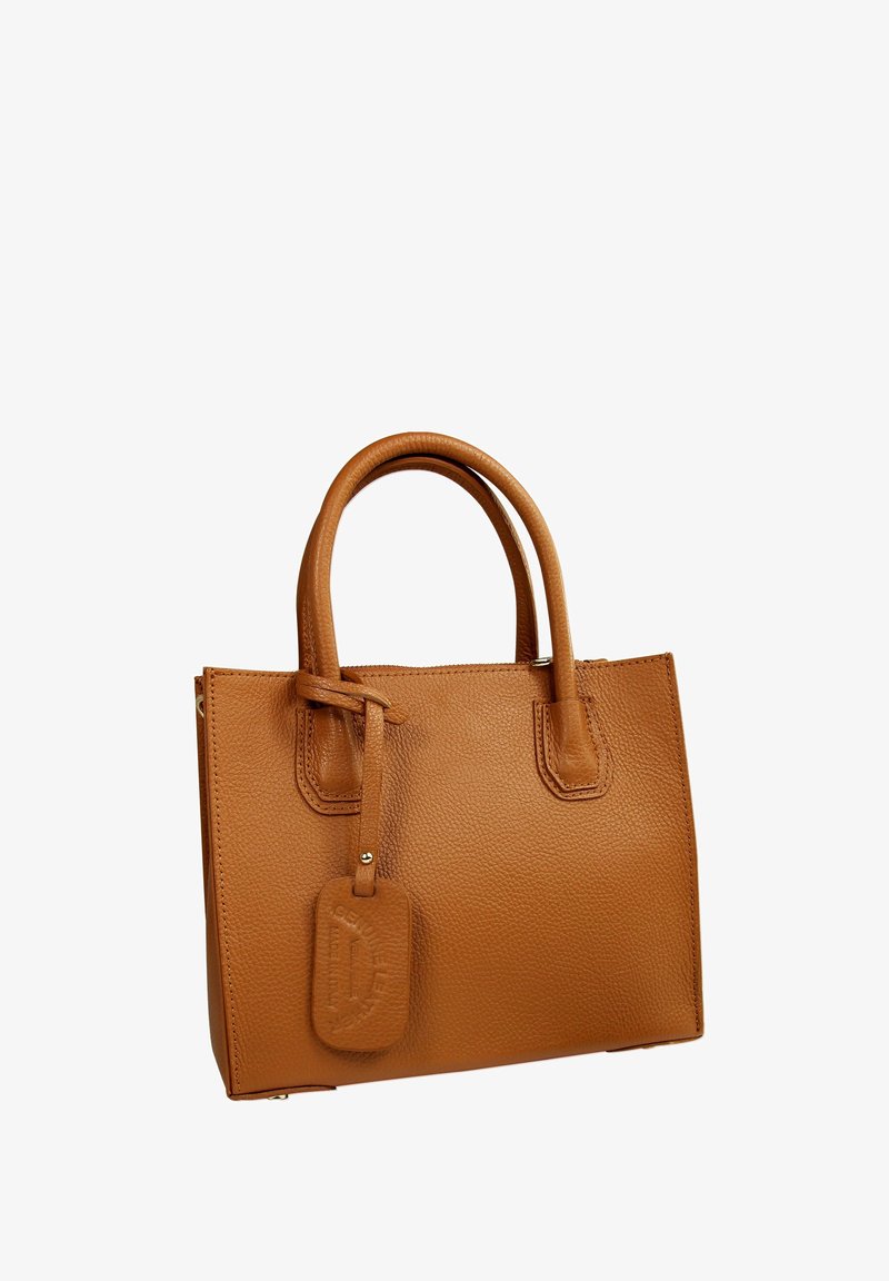 Sac à main en cuir tan avec deux poignées supérieures, finition texturée, forme rectangulaire et une étiquette amovible avec du texte en relief.