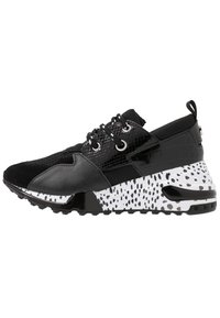 Sneaker nera con texture miste, suola bianca con spruzzi neri, lacci bianco e neri, e un passante sul tallone.