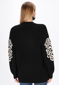 Maglione nero lavorato a maglia con una vestibilità comoda e maniche lunghe, decorato con ornamenti beige sui gomiti. Texture morbida.