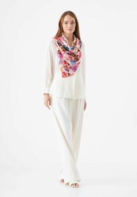 Zijde bloemen sjaal in tinten van roze, blauw en rood, gecombineerd met een witte textuurlijke blouse en brede witte broeken, met een casual pasvorm.