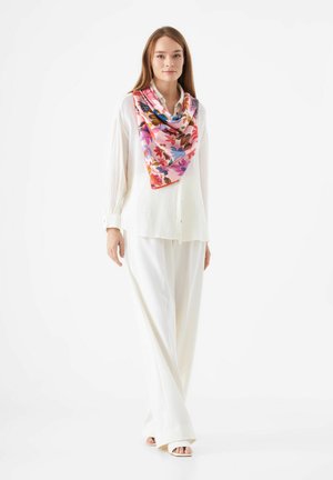 Zijde bloemen sjaal in tinten van roze, blauw en rood, gecombineerd met een witte textuurlijke blouse en brede witte broeken, met een casual pasvorm.