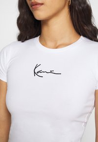 T-shirt en coton blanc au design ajusté, avec un logo brodé noir sur la poitrine et un col ras du cou.