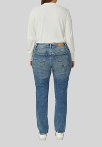 Niebieskie dżinsy z lekkim efektem sprania, o fasonie prostych nogawek i dwoma tylnymi kieszeniami, zestawione z białą, prążkowaną bluzką z długim rękawem.