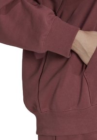 Felpa bordeaux in tessuto strutturato, dotata di tasca a marsupio e polsini a costine. Il design è casual e ha una forma rilassata.