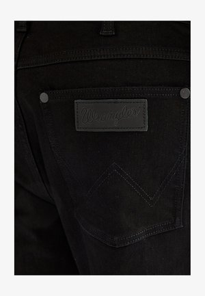 Tylnia kieszeń czarnych jeansów Wrangler z czarną skórzaną naszywką z nazwą marki przeszytą nad kieszenią.