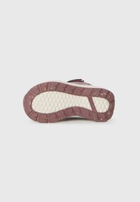 Sola de ténis infantil em castanho e branco com manchas multicoloridas e padrão de ranhura texturizada em fundo simples.