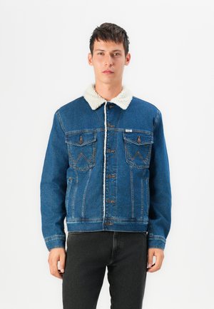 Giubbotto in jeans blu con colletto in sherpa bianco, chiusura a bottoni, due tasche sul petto e design aderente; tessuto testurizzato con dettagli di cucitura visibili.