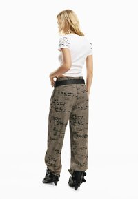 Valge lühikeste varrukatega särk ja mustriga pruunid laiade säärtega püksid kirjastiilsete kujundustega. Must rihm ja läikivad mustad pahkluu saapad.