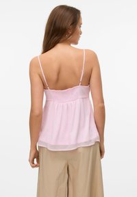 Light pink camisole with thin straps and smocked bodice detail. Loose fit and layered design, made from lightweight fabric, casual style.