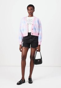 Cárdigan de argyle en rosa y azul pastel con botones, combinado con una camiseta gráfica blanca, pantalones cortos desgastados negros y un bolso negro.
