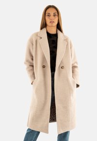 Abrigo de mezcla de lana beige con solapas anchas, doble botonadura, bolsillos laterales y un exterior texturizado; cuenta con un forro de estampado de leopardo.