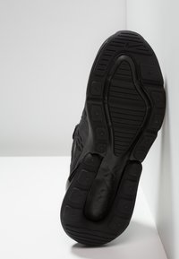 Chaussure de sport noire avec un dessus en mesh texturé, dotée d'une semelle en caoutchouc avec un motif de crampons et d'une légère élévation au niveau du talon.