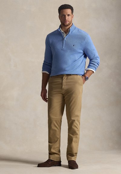 Ανοιχτό μπλε πλεκτό πουλόβερ με φερμουάρ, χακί παντελόνια και καφέ μοκασίνια. Το πουλόβερ έχει ριμπ γιακά και μανσέτες. Απλός σχεδιασμός.