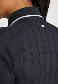 Must või mustriline särk vertikaalsete triipudega, musta kraega, millel on valge ääre ja seljal väike valge logo.