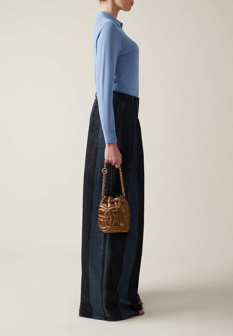 Light blue long-sleeve top, dark denim wide-leg pants with vertical stripes, and a textured gold bucket bag with a chain handle.
