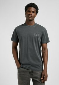 Camiseta de algodón gris oscuro con cuello redondo, mangas cortas y un pequeño logo "LEE" en gris claro en el lado izquierdo del pecho. Textura suave.