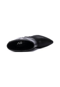 Bota de tobillo de cuero negro con punta afilada, suela plana y cremallera lateral para el cierre; presenta una textura suave y un diseño minimalista.
