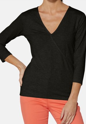 Schwarzes V-Ausschnitt Langarmoberteil mit strukturiertem Muster und überkreuztem Design, kombiniert mit korallfarbener Hose.