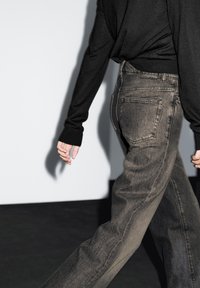 Dunkelgraue Jeans in einer lässigen Passform mit subtilen Verwaschungen, Gesäßtaschen und einem strukturierten Stoff, kombiniert mit einem schwarzen Langarmoberteil.