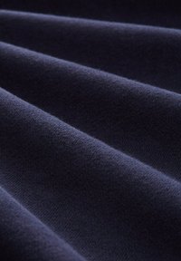 Tessuto blu navy con una consistenza morbida, caratterizzato da molteplici pieghe che creano un motivo ondulato. La superficie è uniforme senza imperfezioni visibili.