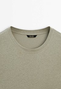 Gros plan d'un t-shirt gris clair à col rond en tissu lin-coton avec coutures visibles au col et étiquette de marque à l'intérieur de l'encolure.